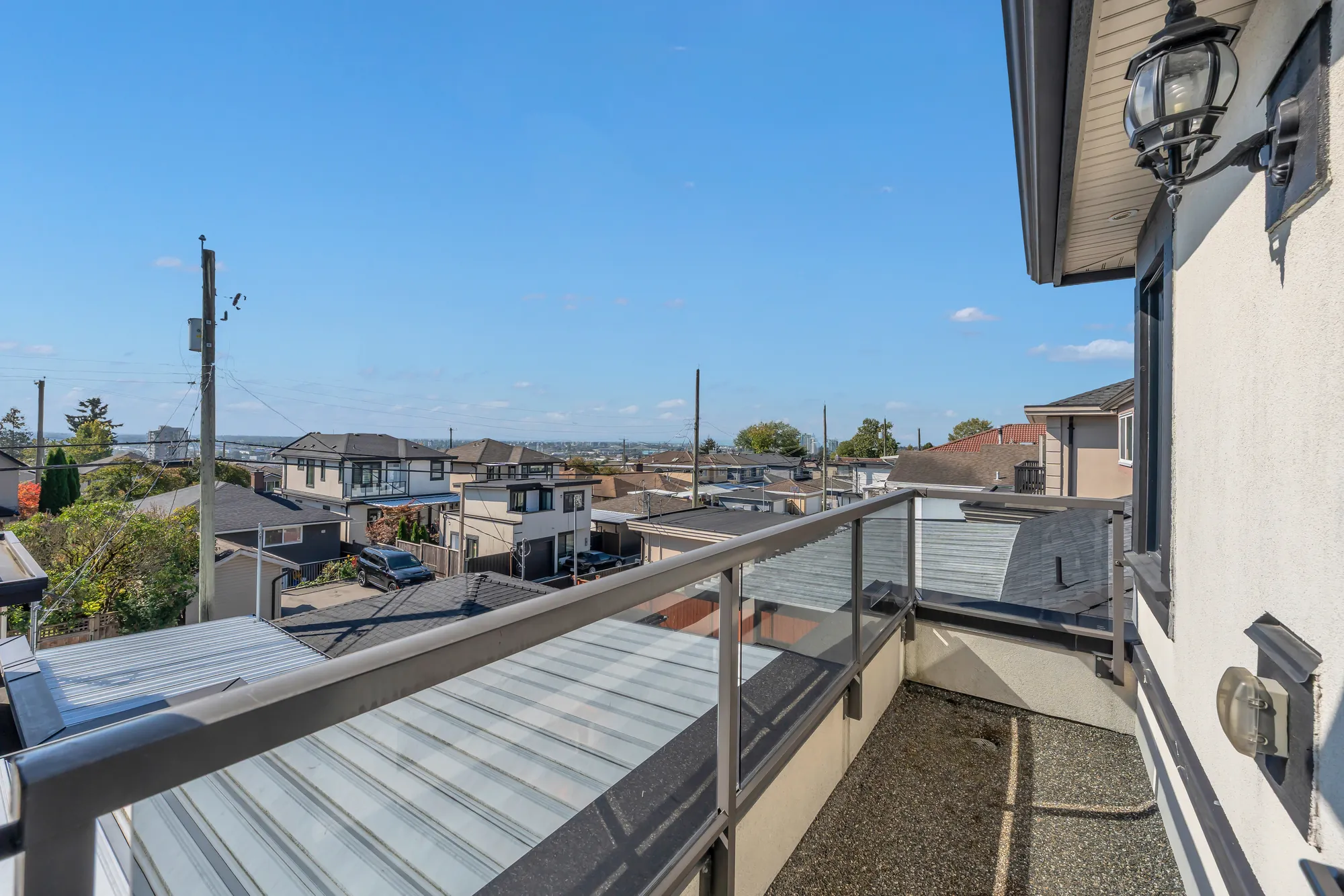 The small balcony upstairs: a glass railing, the roof of the covered balcony below, the rooftops and the flat land to the south
