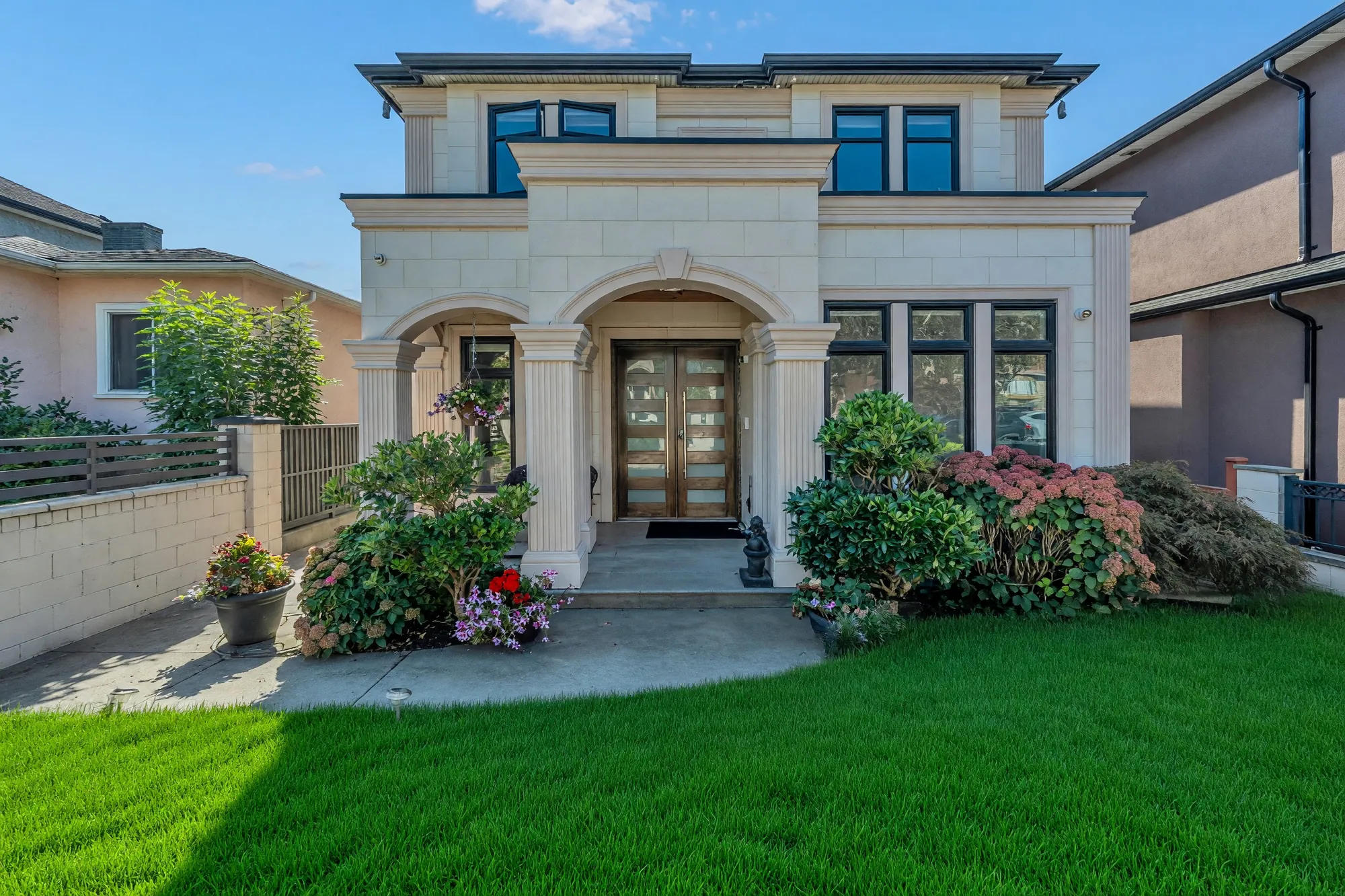The front of the house from the walk: cream limestone, an arched portico on square columns over a wood-and-glass door, shrubs either side, the lawn shown green