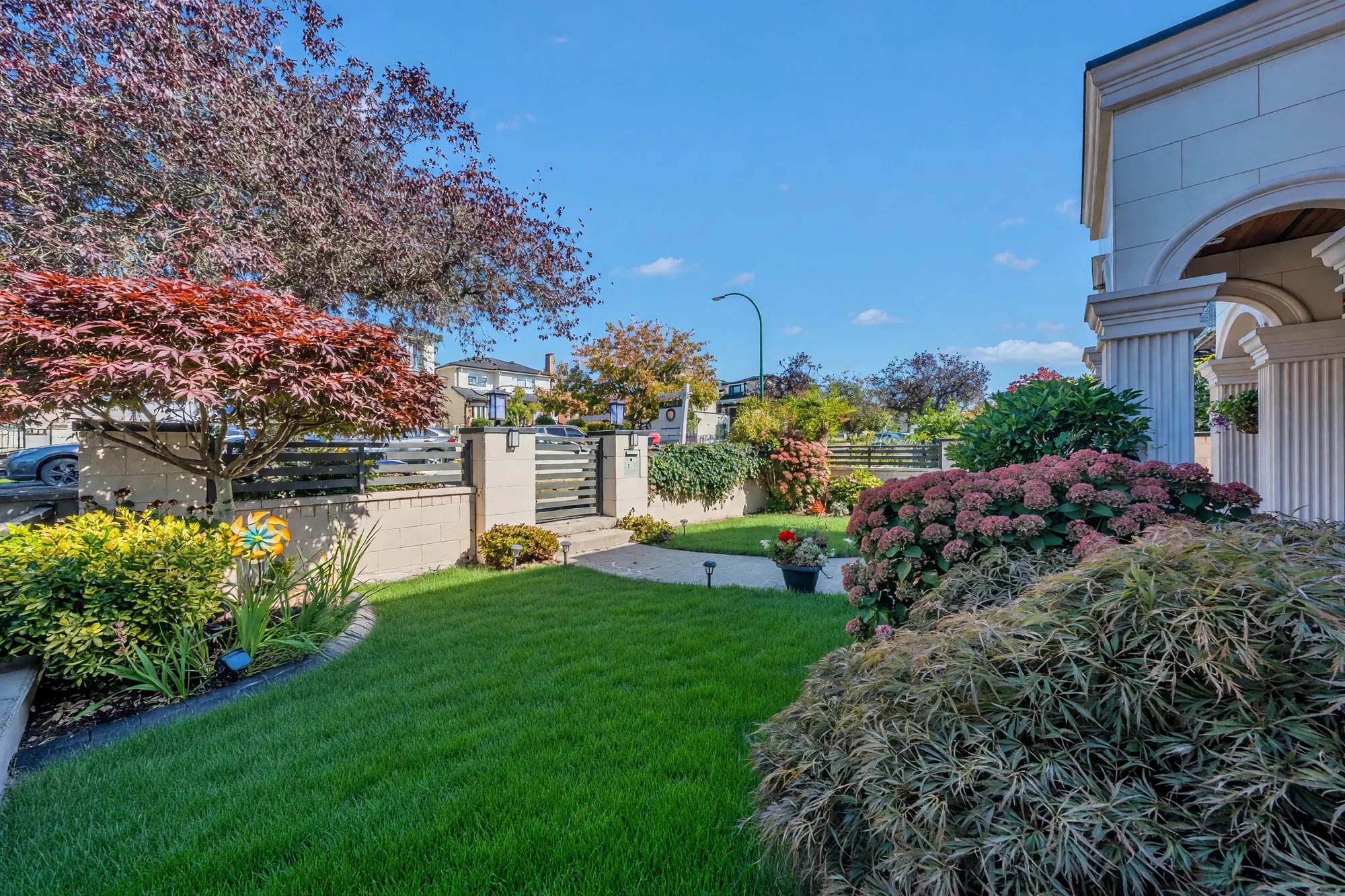 The front garden: the lawn between hydrangeas and a Japanese maple, the wall and gate to the street, the portico's column at the right