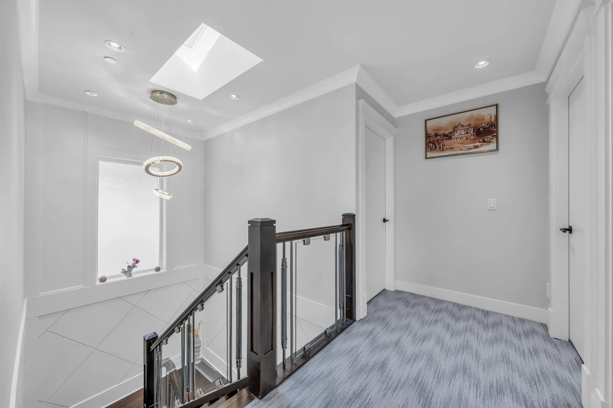 The landing: a skylight and a crystal ring pendant over the stair's dark rail, a niche with a vase, grey carpet, doors to the bedrooms