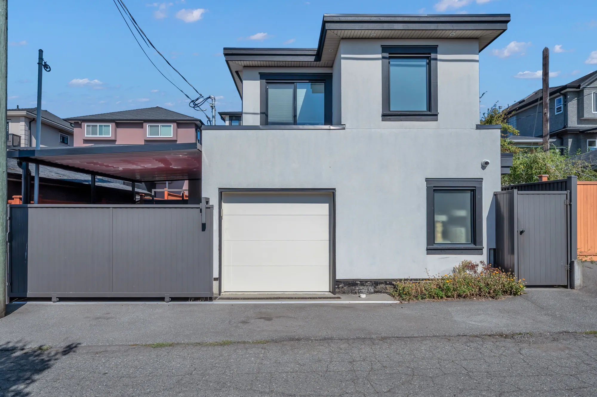 From the lane: the laneway house over a white garage door, the carport's gate beside it, the neighbours' garages