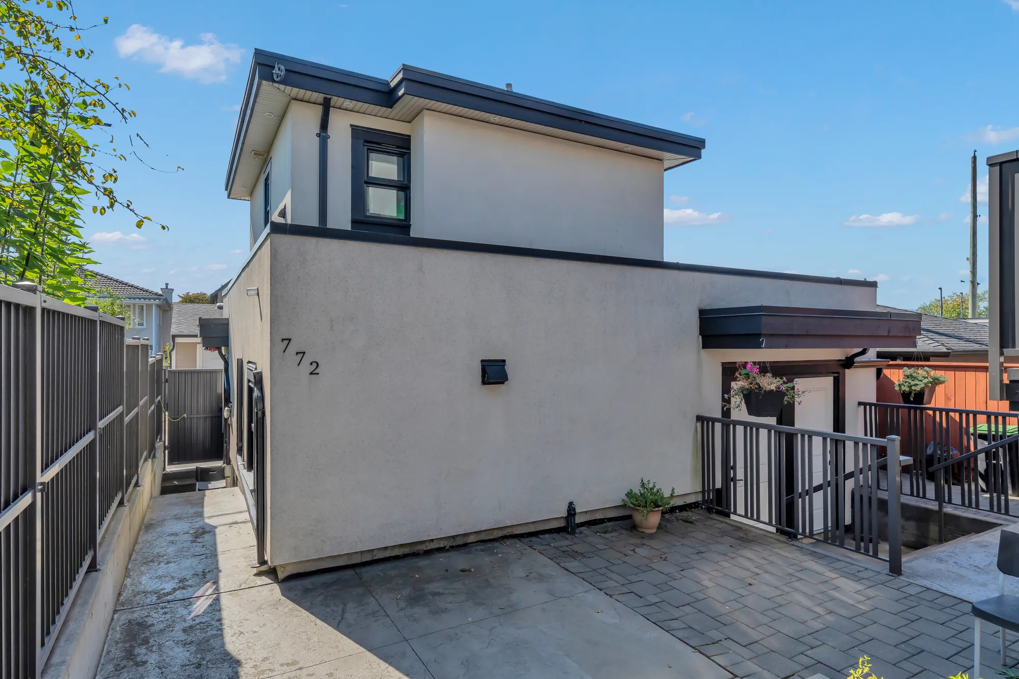 The laneway house from the courtyard: two storeys of white stucco under a flat roof, a window above, a door and a railing below, the paved courtyard in front