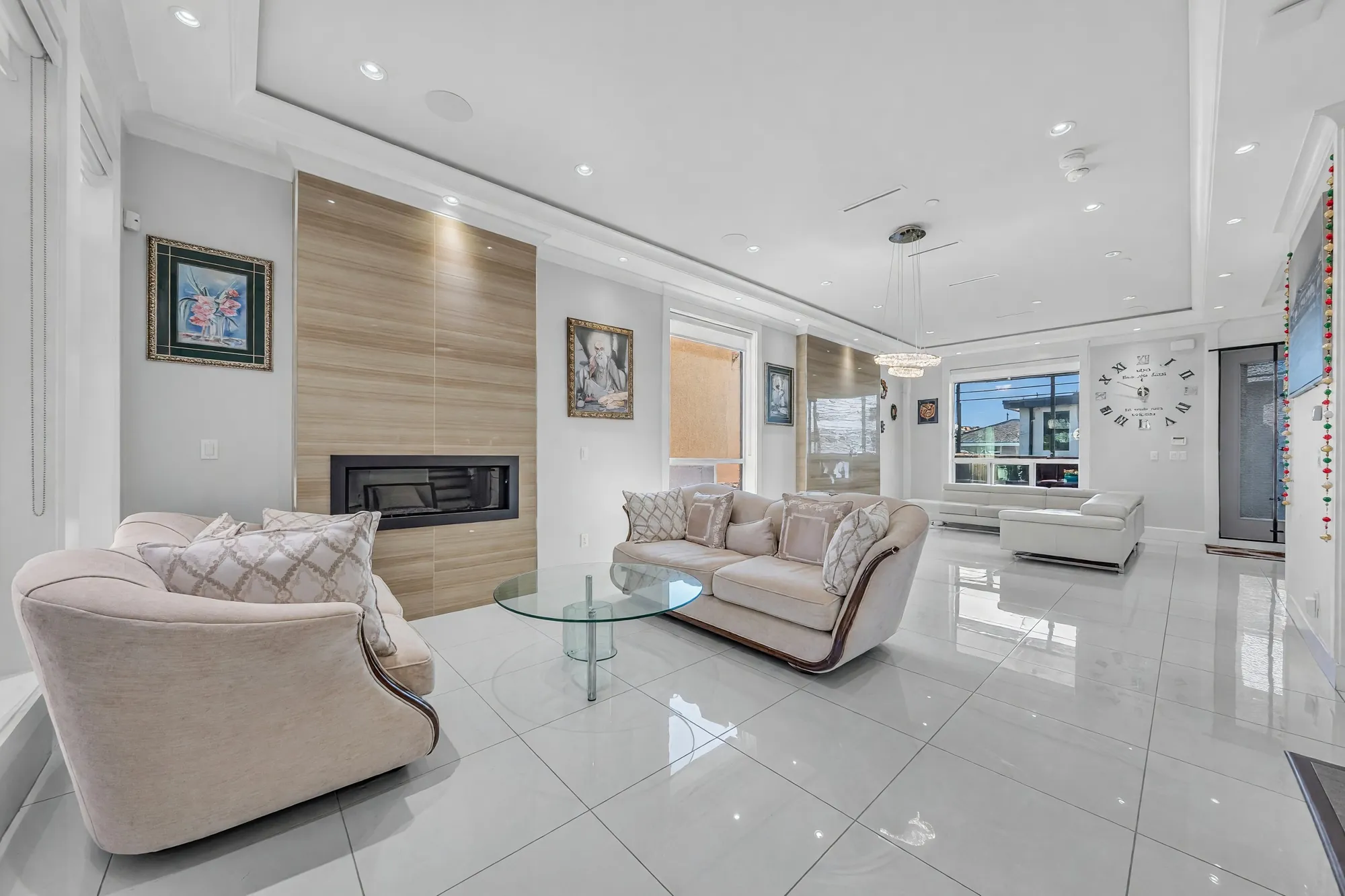 The living room: cream sofas with wood trim around a glass table, the fireplace in the pale wood wall, the dining room and the family room beyond