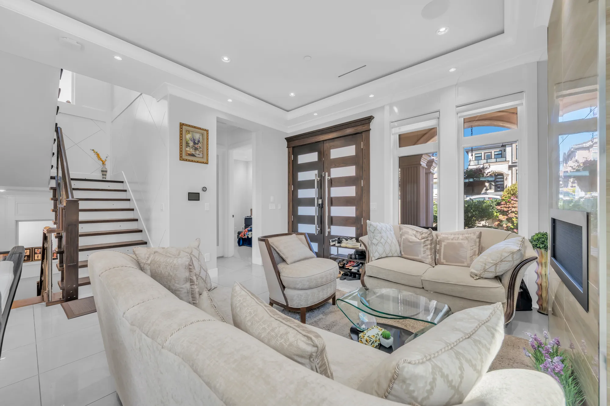 The living room from the stair: the sofas, the glass table, the front doors and the tall windows