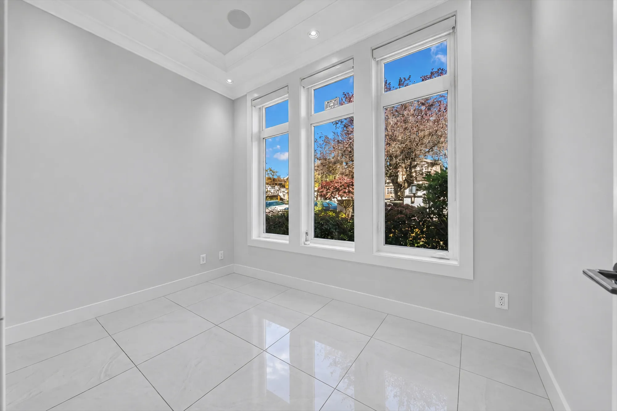 The office shown empty: white tile, three tall windows to the street with a maple outside, a tray ceiling