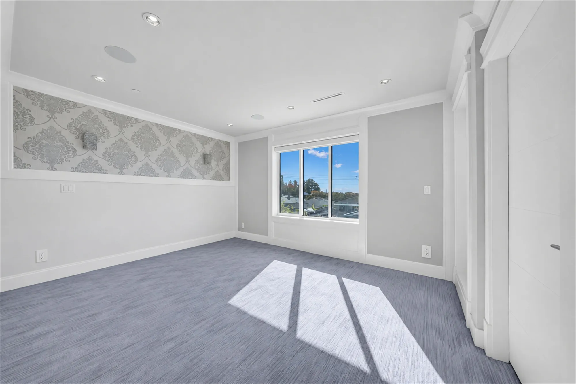 The primary bedroom from the door, shown empty: the damask feature wall, the window, the closet's doors