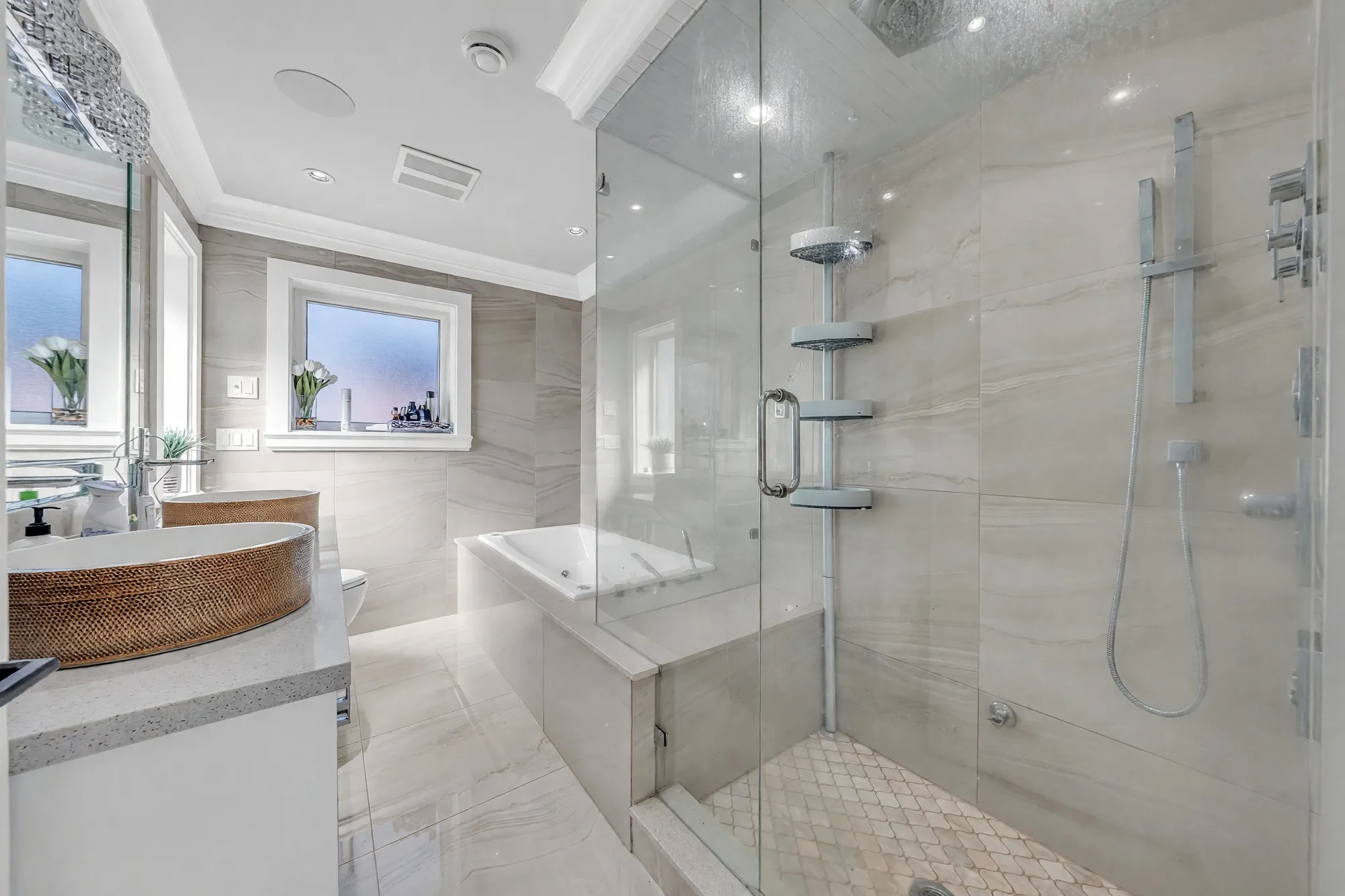 The primary bathroom: a rattan-wrapped basin on a quartz counter, a soaker tub under a window, a glass shower with a rain head, stone-look tile