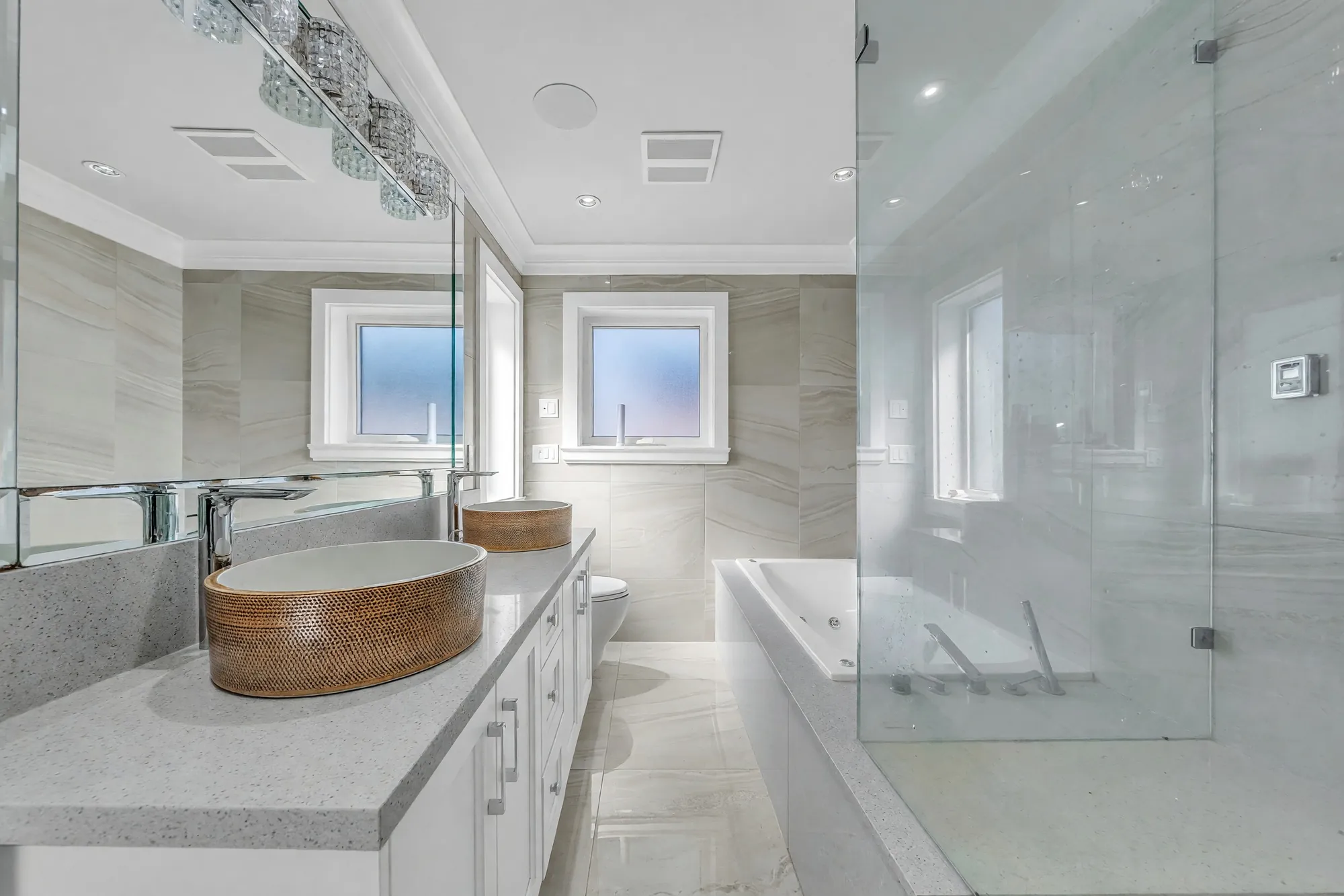 The primary bathroom from the door: the long vanity with its basin, the mirror wall, the tub and the shower beyond, a crystal light bar