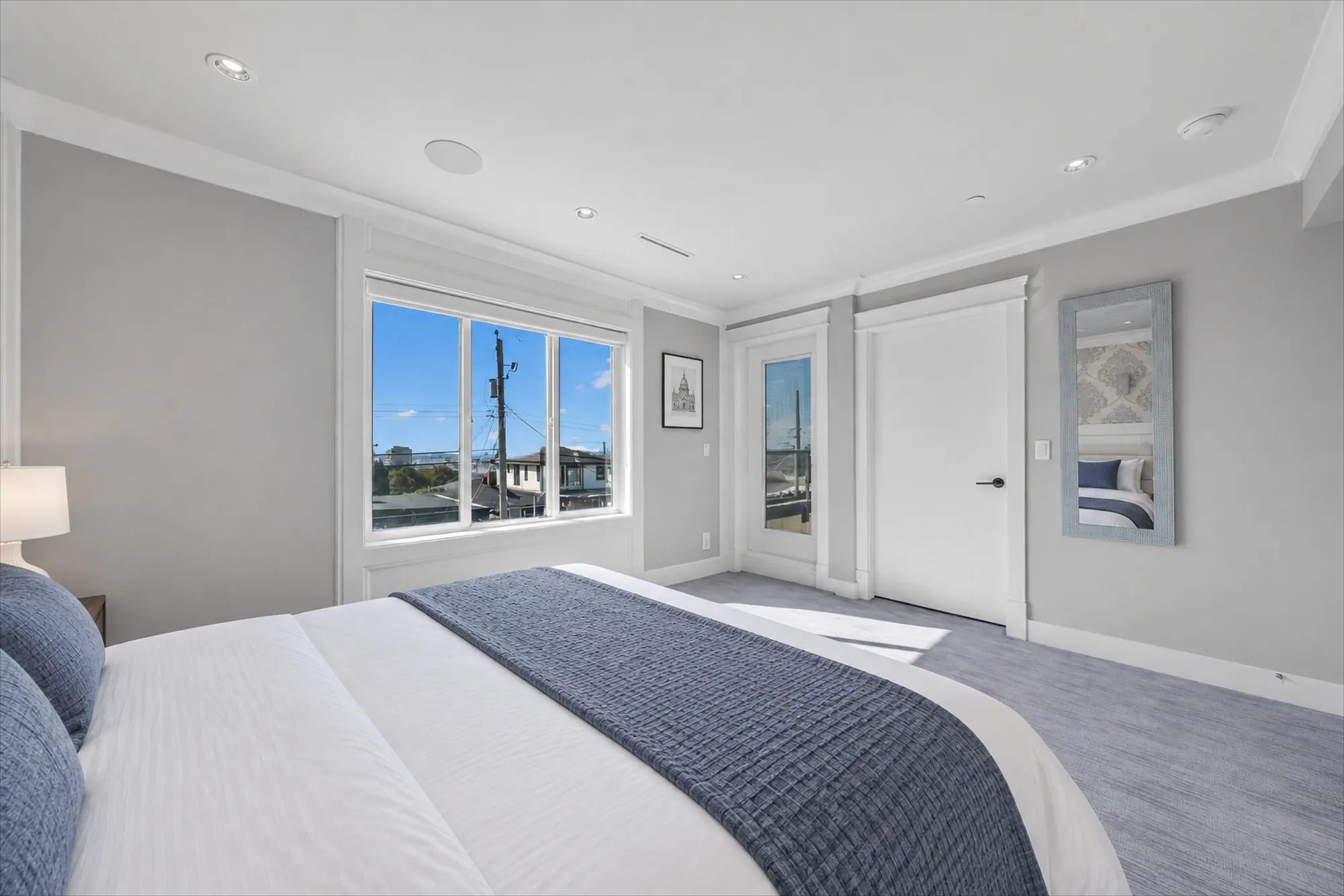 The same view virtually staged: a bed with a grey throw, a night table and lamp, pictures on the walls