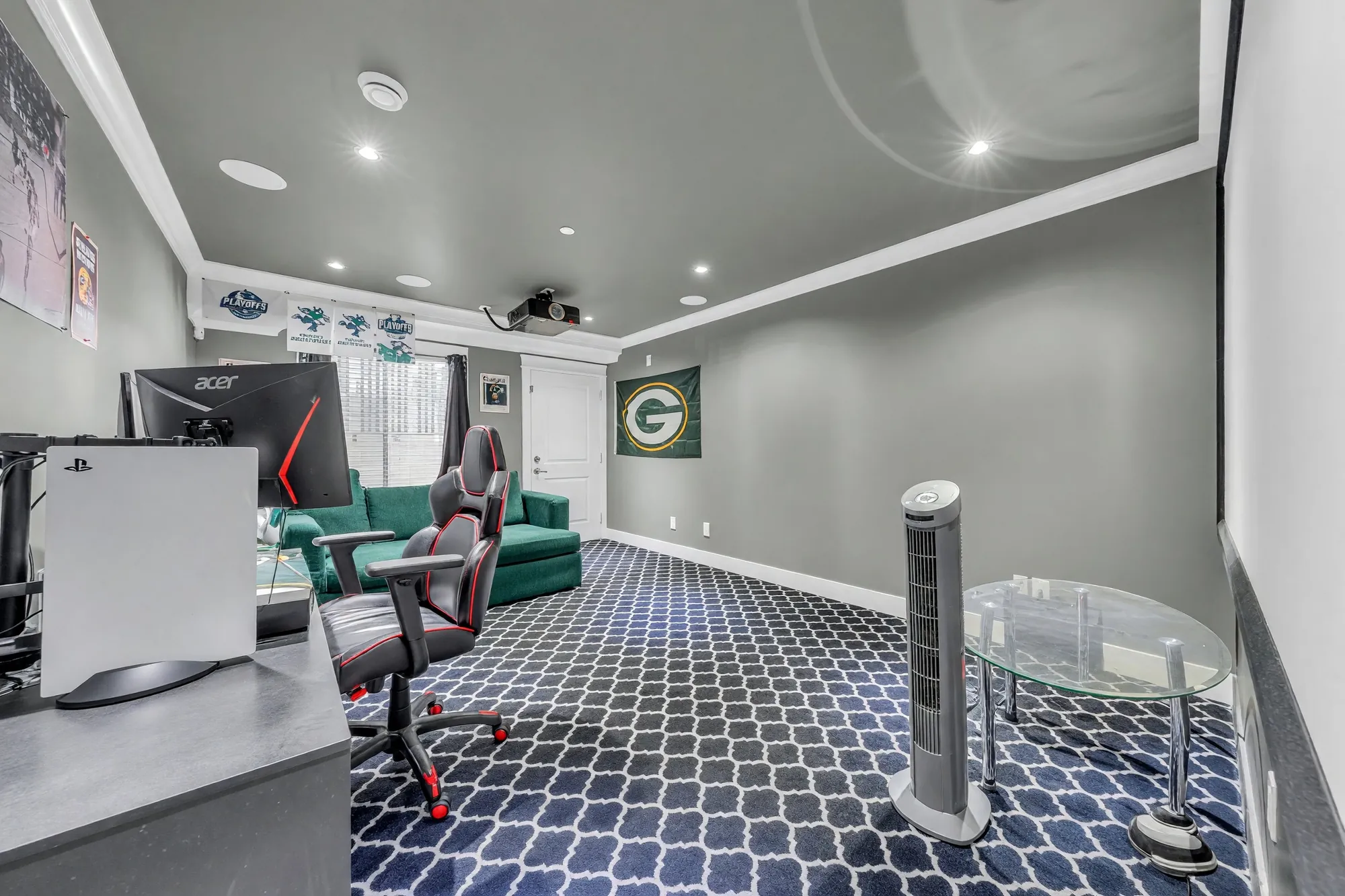 The sitting area: a patterned carpet, a green armchair, a desk with a monitor and a gaming chair, grey walls, pot lights