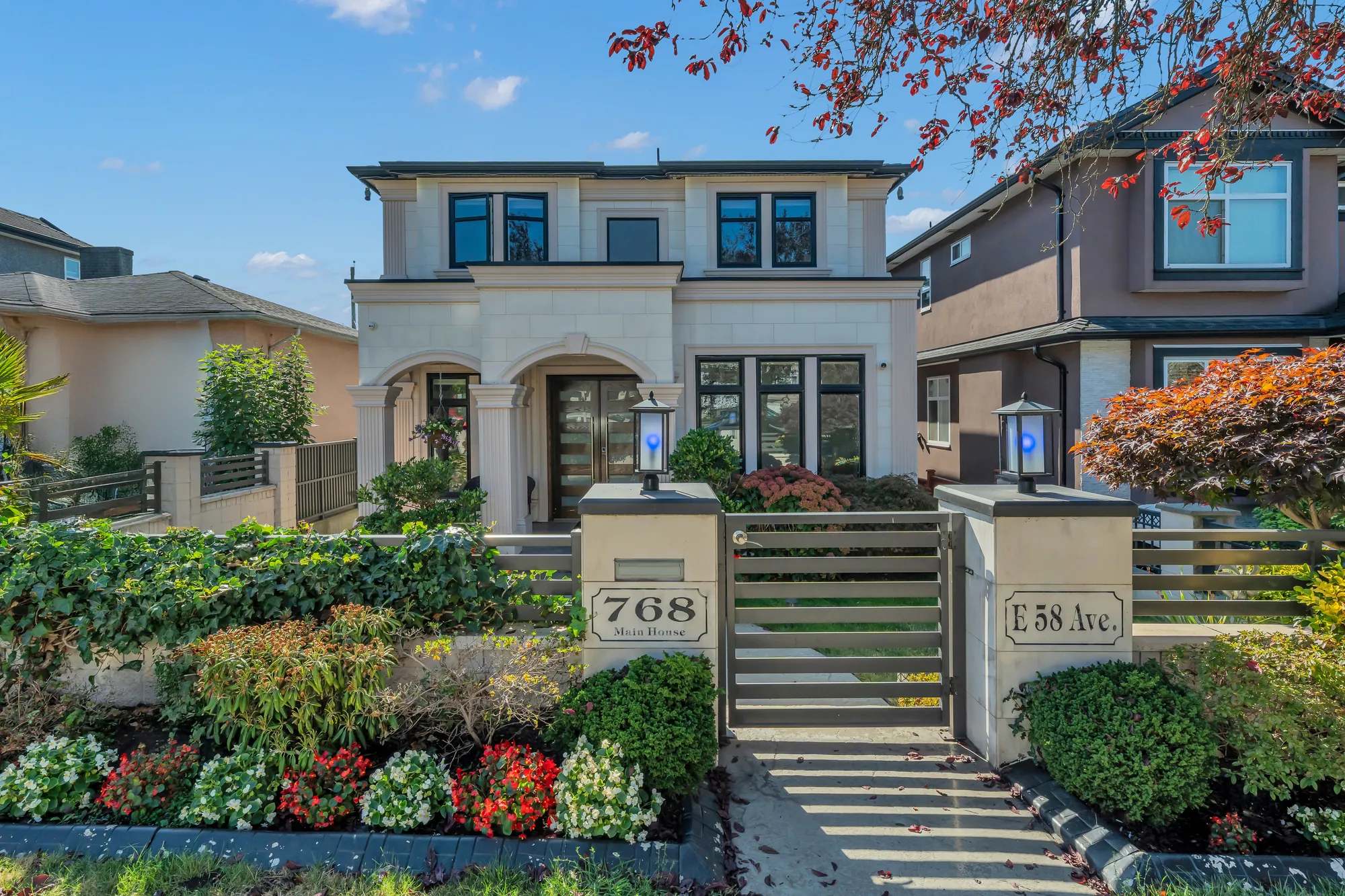 The house from the street: the limestone gate piers with the number 768 and E 58 Ave, the slatted gate, the steps up through the front garden, the portico and the upper windows, a red maple at the corner