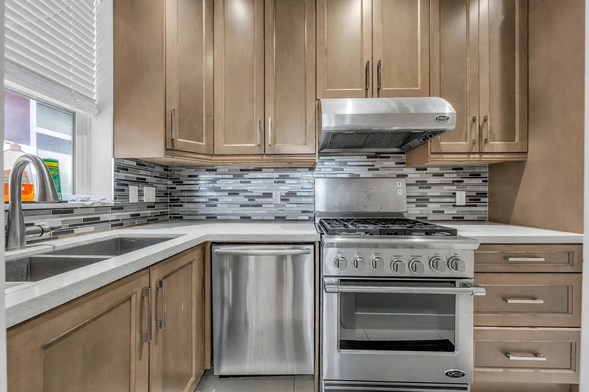 The wok kitchen: maple cabinets, a gas range under a hood, a mosaic backsplash, a sink under the window